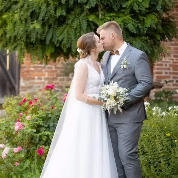 Brautpaar küsst sich vor einer Ziegelmauer mit Rosen